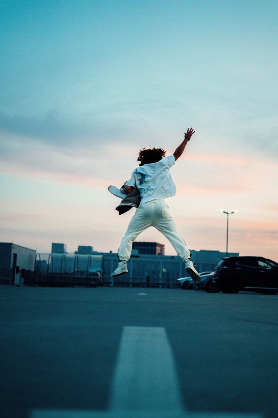 David springt als Silhouette gegen den Abendhimmel auf einem Parkdeck